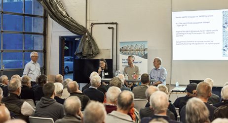 2026 09 30 Deltagere Sidder Tæt I Vejle Spildevands Garage, En Kvinde Taler I Mikrofon Ved Et Vejle Spildevand