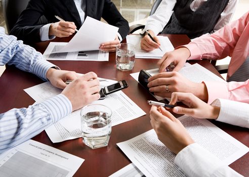 mødebord med deltagere papirer mobiler og kuglepenne.jpg